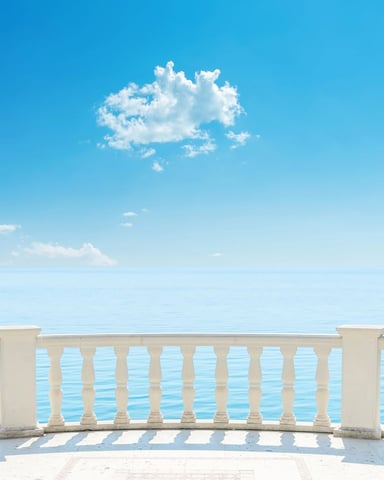 Curved white stone balustrade overlooking calm blue sea under clear sky with white clouds