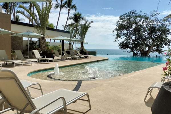 Beachfront infinity pool with loungers, umbrellas, palm trees, and ocean view