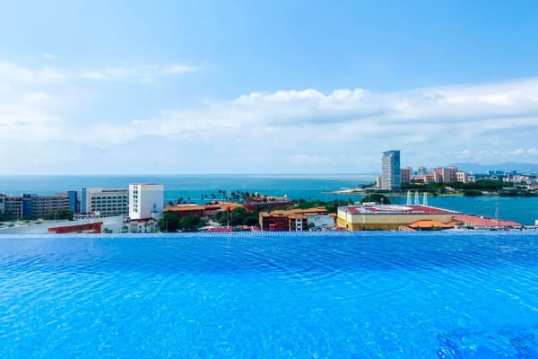 Infinity pool overlooking coastal city with high-rise hotels, ocean, and mountains in distance
