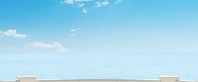 White stone balustrade overlooking calm blue sea and sky with white clouds